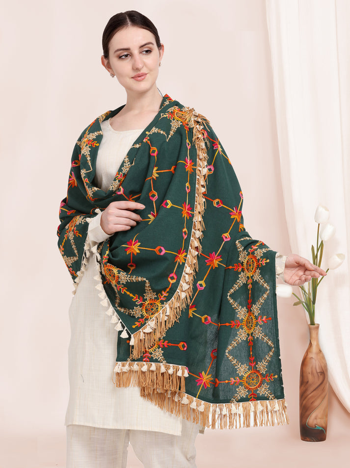 Woman holding a green shawl with intricate patterns and fringes.