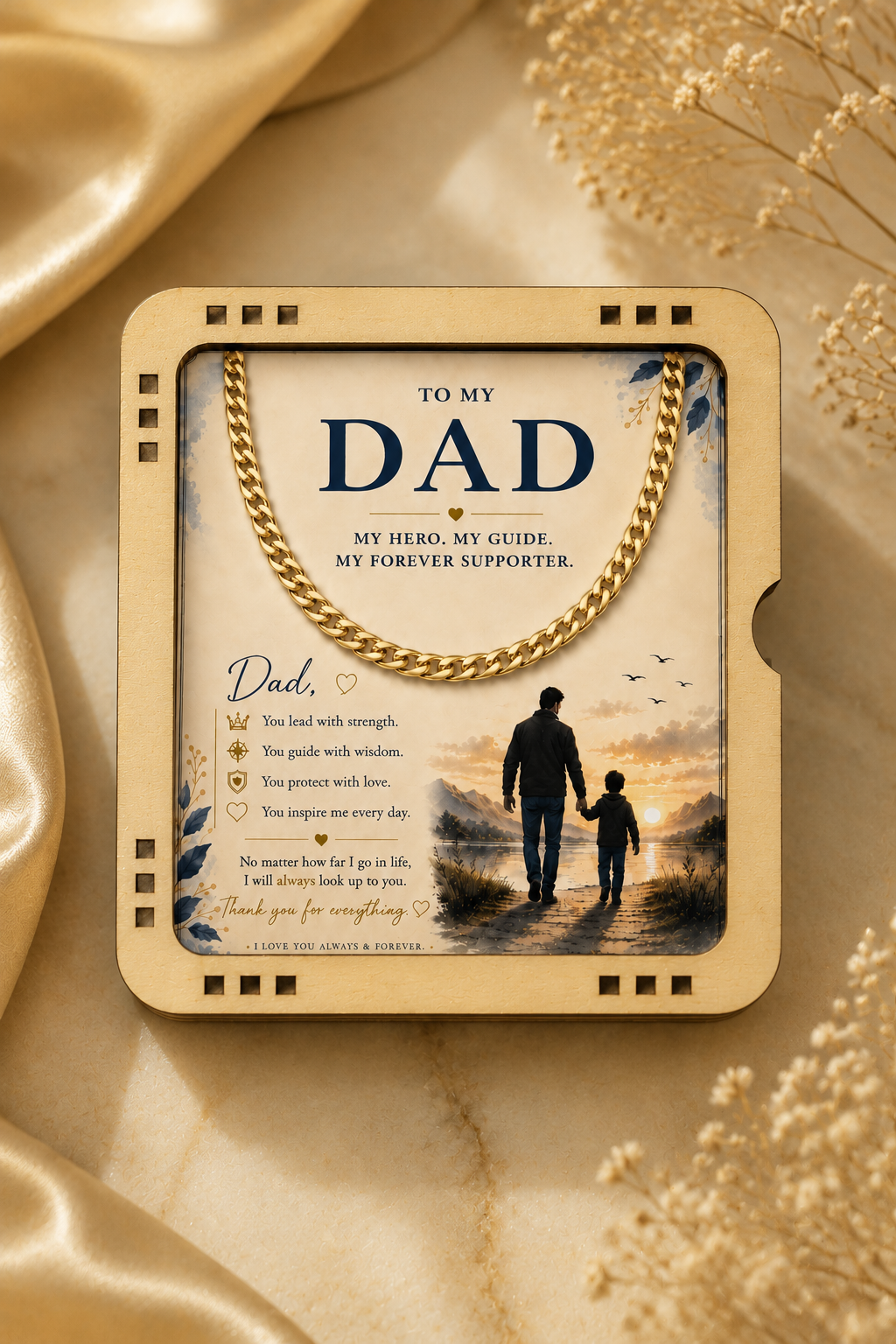 A framed personalized gift box for Dad, styled on a gold satin fabric background with dried flowers. The box features a gold chain handle and a printed card with a silhouette of a father and child, along with a list of memories and a quote.
