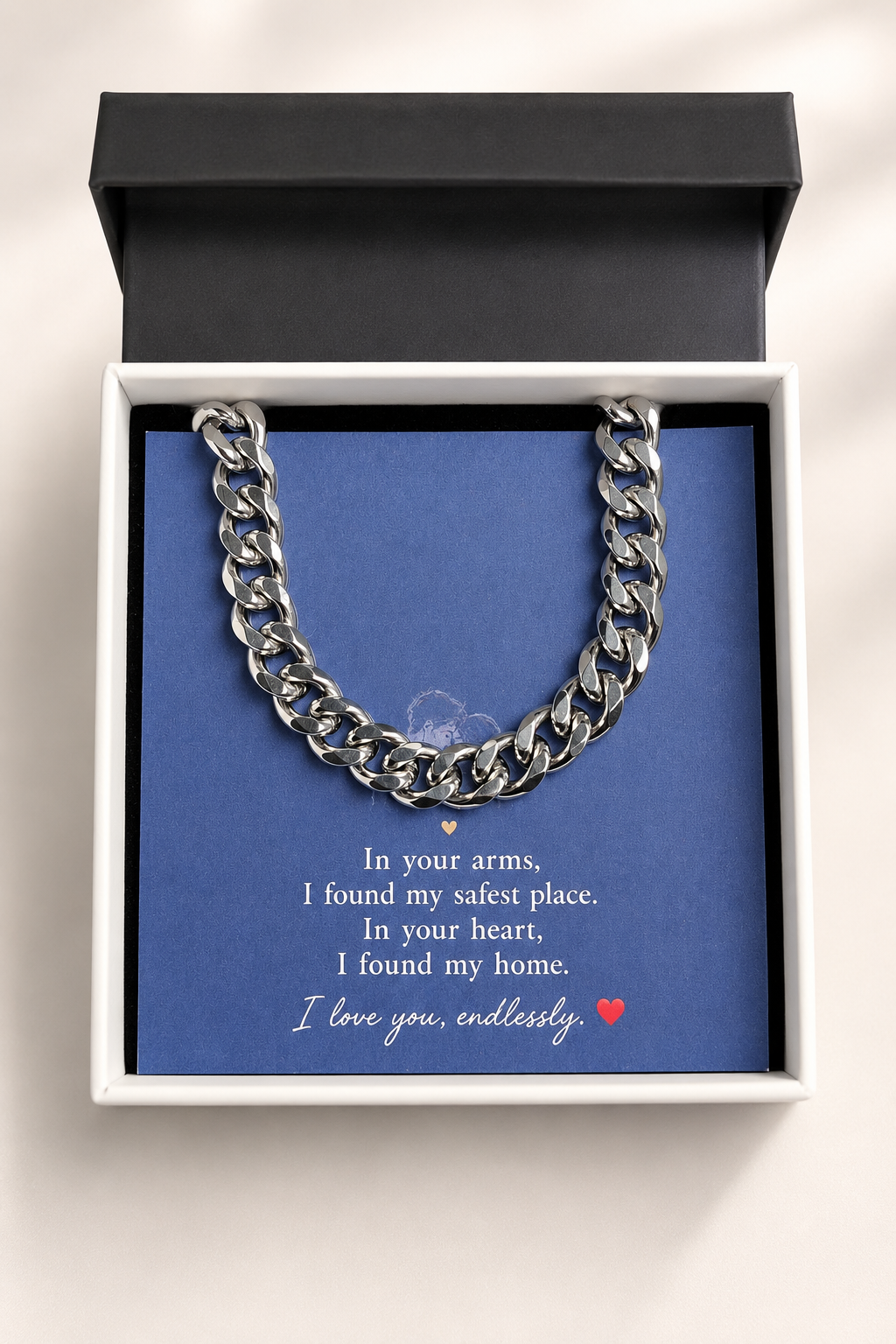 A silver Cuban link chain necklace presented inside an open white gift box with a black lid, set against a blue card with a sentimental message printed on it.