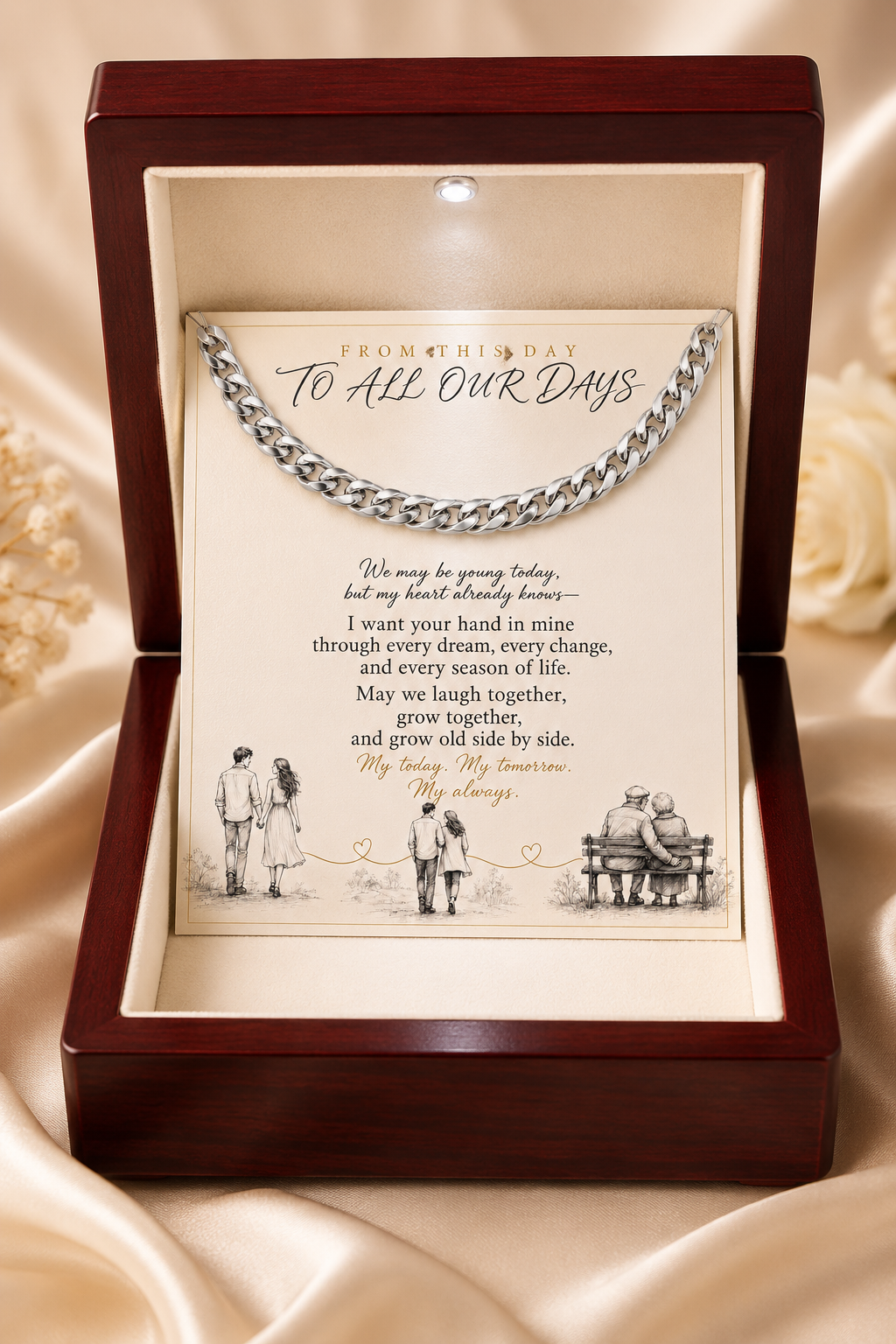 A silver chain necklace presented inside an open dark wood keepsake box with a cream insert. The card includes a printed quote starting 'From this day to all our days' and small black-and-white illustrations, set against a draped satin fabric background.