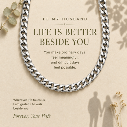 A silver curb chain necklace arranged in an oval on a warm beige background with printed sentimental text for a husband and decorative dried leaves and shadow overlays.