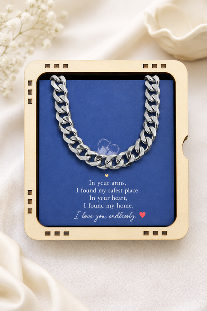 A silver curb chain necklace presented inside a square cream-colored gift box with a blue insert card. The card features a romantic poem about the chain and is styled on a soft cream fabric background with decorative dried flowers.