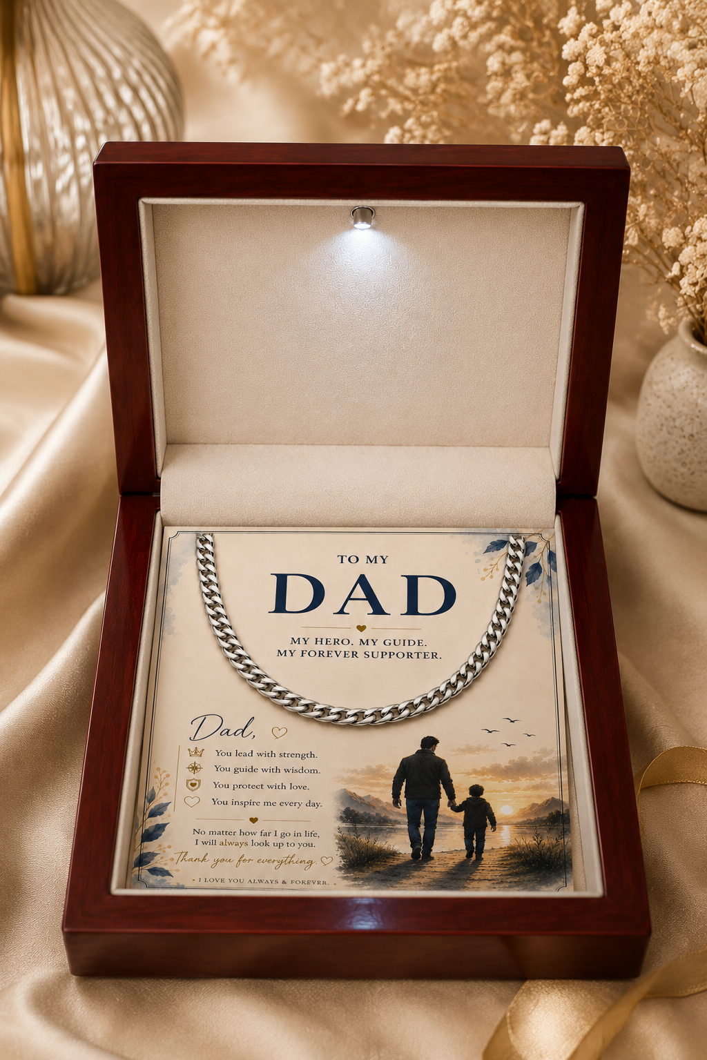 An open dark wood keepsake box on draped satin fabric, displaying a silver chain necklace over a printed card addressed 'TO MY DAD' with a family silhouette illustration.