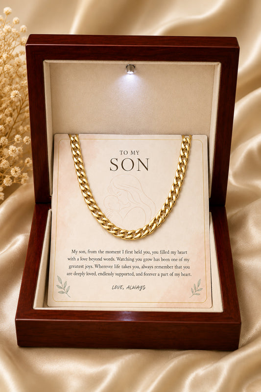 A gold-colored chain necklace presented inside an open dark wood gift box with a cream message card addressed 'TO MY SON,' set on a satin fabric background.