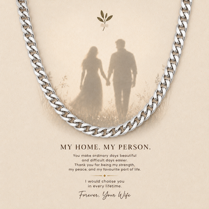 A silver curb chain necklace draped over a beige memorial-style card with a faded silhouette of a couple holding hands and the text 'MY HOME. MY PERSON.