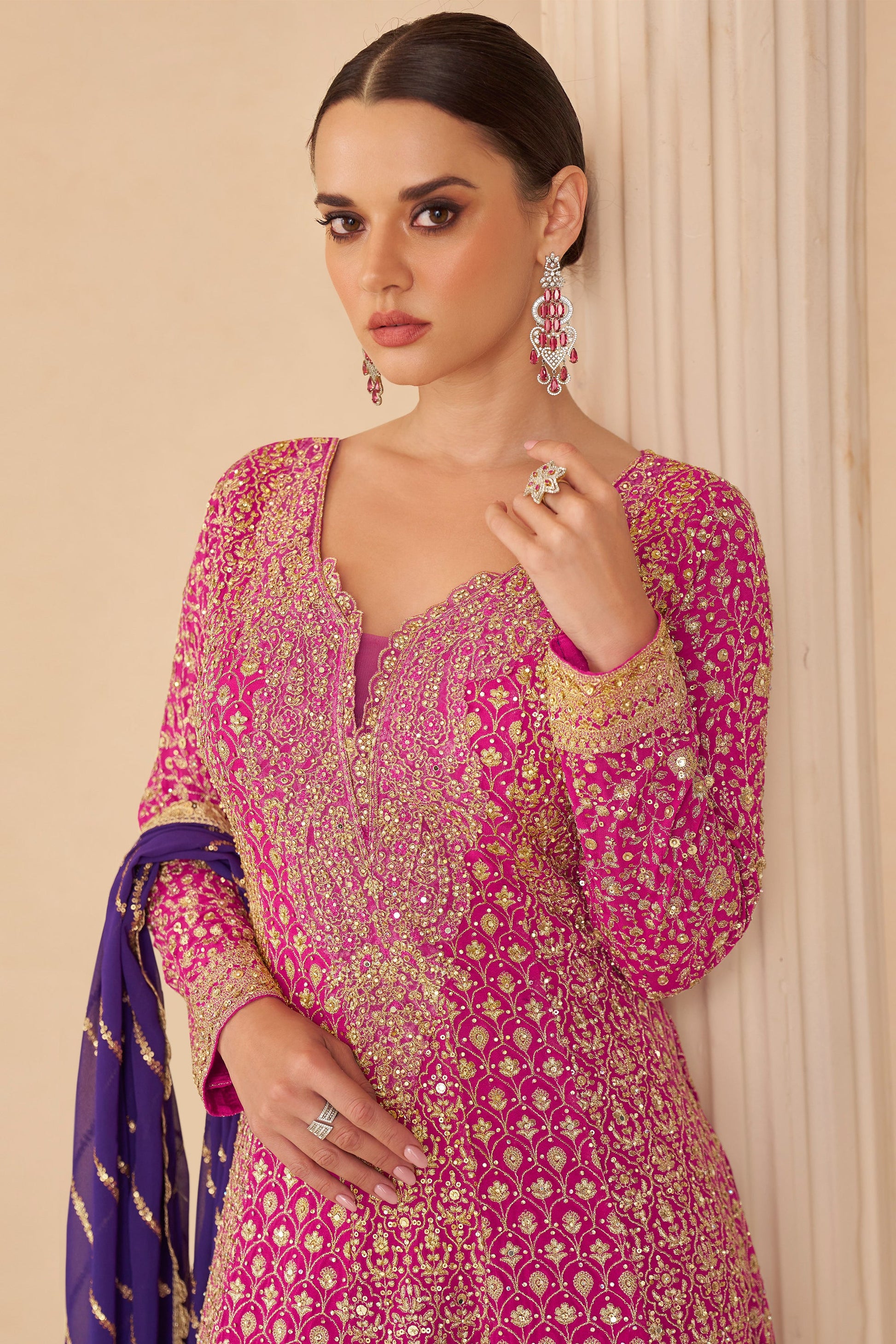 Woman wearing a pink and gold embroidered traditional outfit with a purple dupatta.