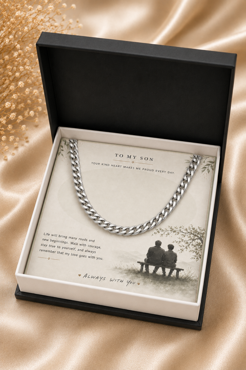 A silver-toned chain necklace presented inside an open black gift box with a cream insert card addressed 'TO MY SON,' set on a satin-like beige fabric background.