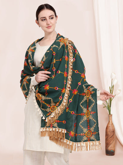 Woman holding a green shawl with intricate patterns and fringes.