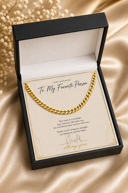 A gold curb-link chain necklace presented in an open black gift box with a cream message card that reads 'To My Favorite Person.' The box is photographed on a champagne satin fabric background with dried flowers at the upper left.