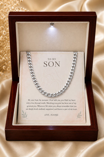 A silver curb link chain necklace presented inside an open dark wood gift box with a cream insert card addressed 'TO MY SON' and a short message, set on a champagne satin background.