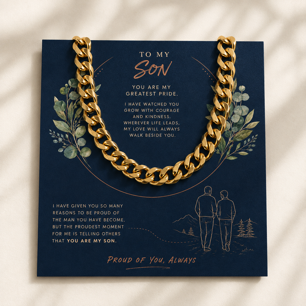 A gold chain necklace draped over a navy blue gift card with sentimental text and illustrations, photographed on a light beige surface with soft shadows.