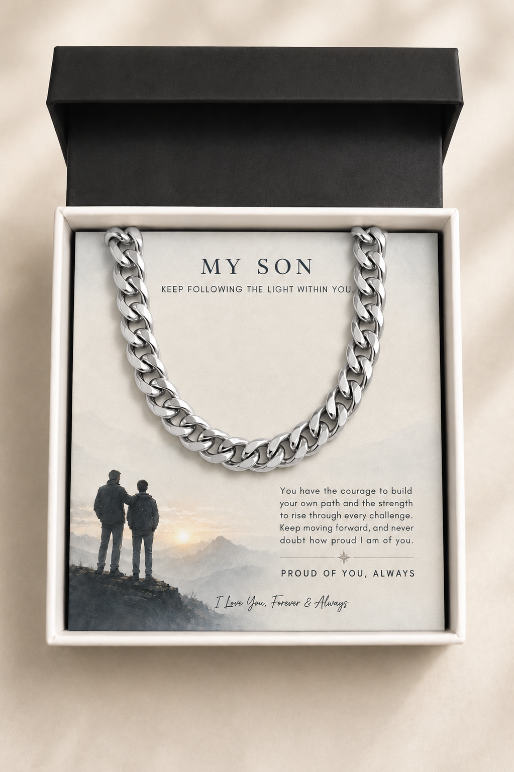 A silver-toned chunky curb chain necklace presented in an open gift box with a printed message card addressed 'MY SON' and a black lid, photographed on a light neutral background.
