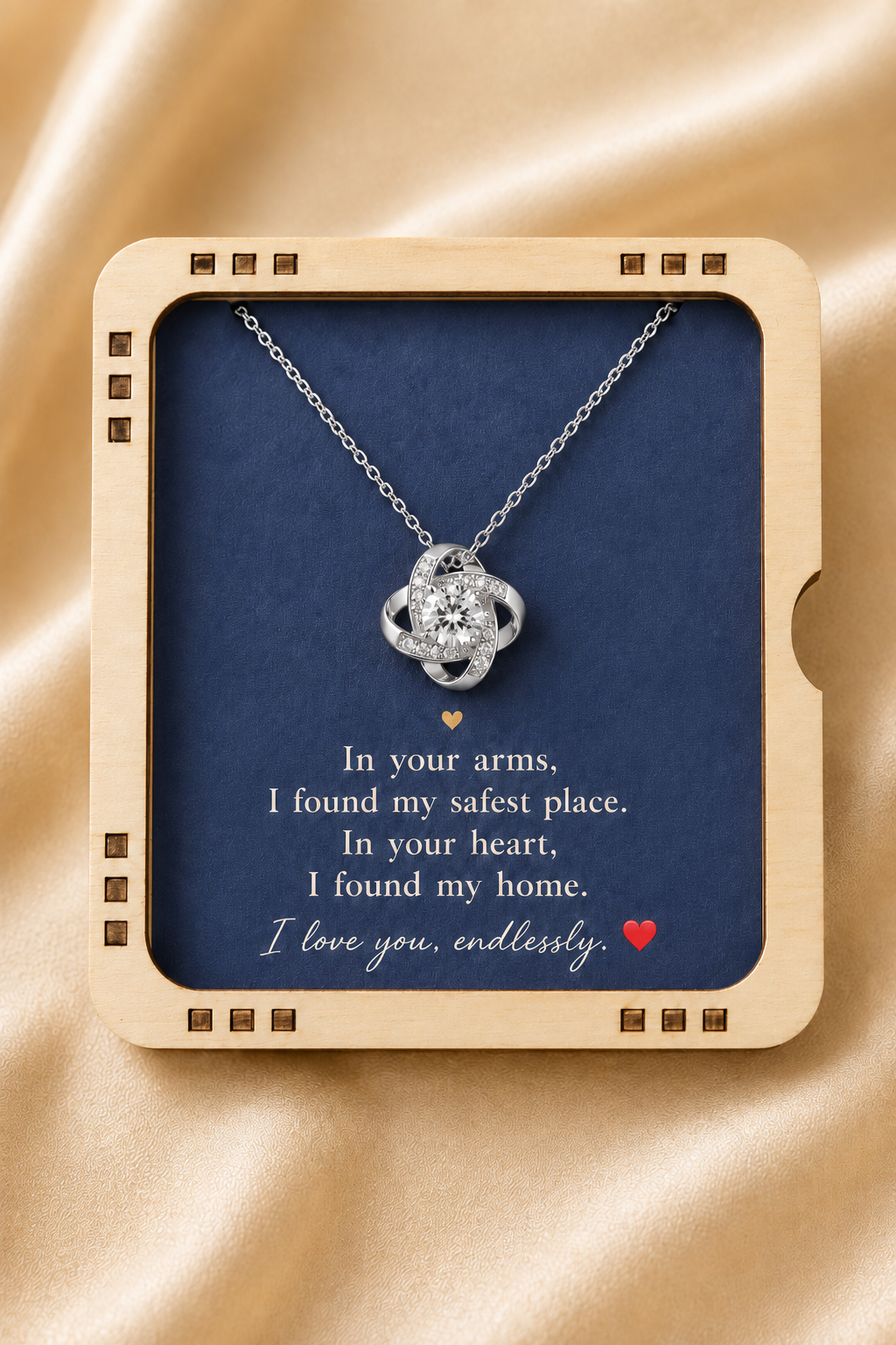 A silver-toned heart-shaped pendant necklace displayed inside a square cream-colored gift box with a navy blue insert. The insert features a sentimental quote printed in white script and block text, with a small red heart at the bottom.