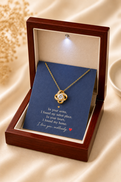 Gold-tone knot pendant necklace displayed on a navy romantic message card inside an open white and black gift box.