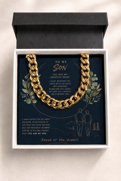 A gold chain necklace presented inside an open white gift box with a black lid, placed on a dark navy card with sentimental text and floral illustrations. The card reads 'TO MY Son' and 'Proud of You, Always.