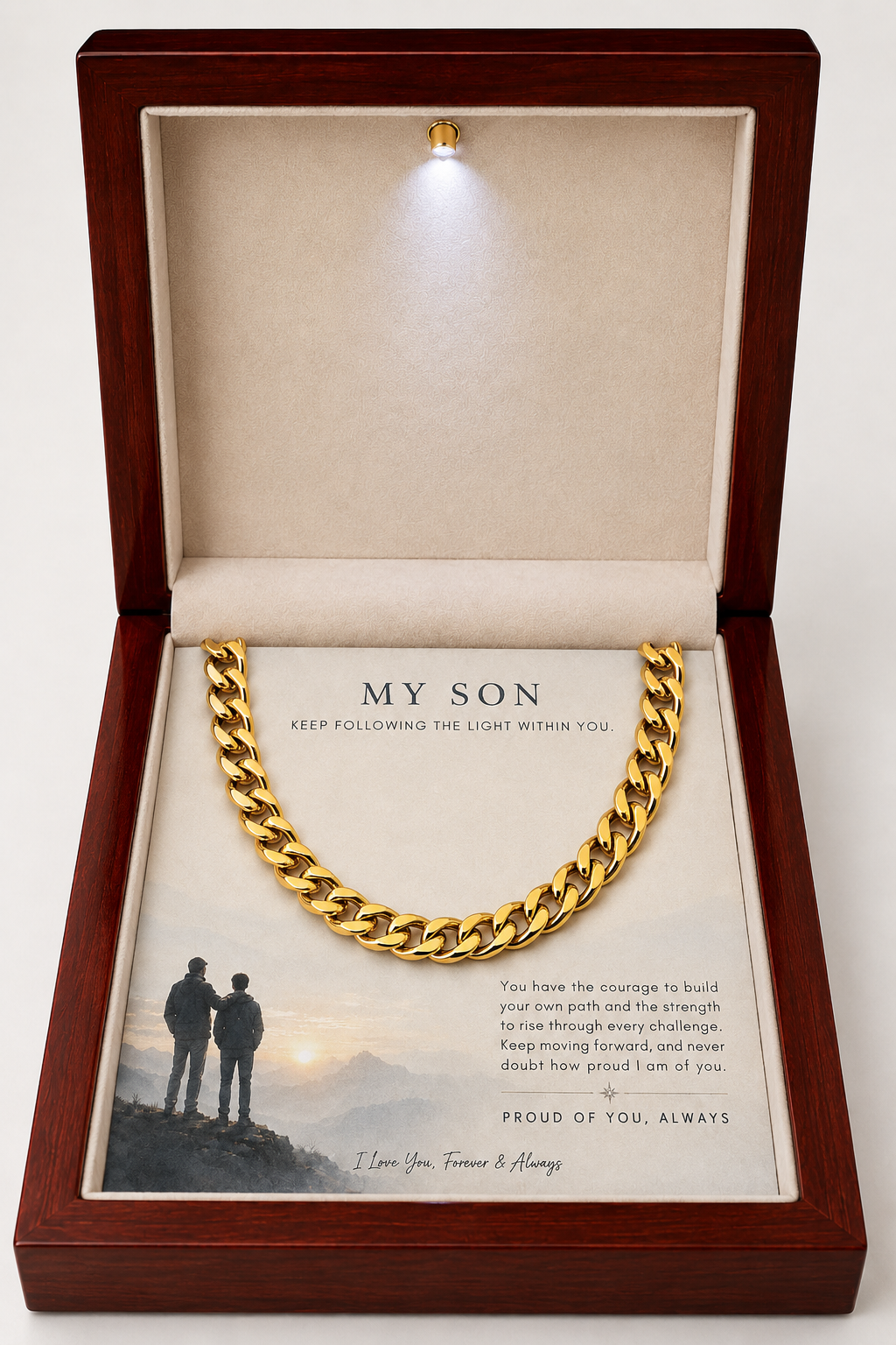 A gold Cuban link chain necklace presented inside an open wooden gift box with a soft cream lining and a printed message card addressed 'MY SON.' The box includes a small built-in light at the top, and the necklace is displayed prominently against a plain light background.