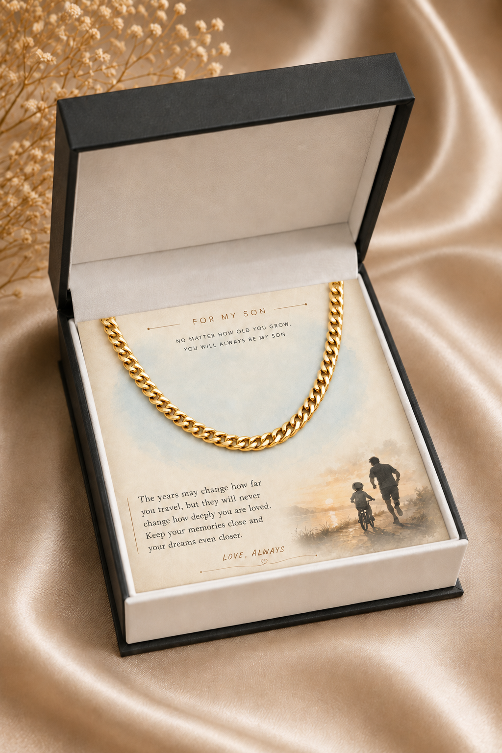 A gold chain necklace presented inside an open black gift box with a printed sentimental card for 'my son,' placed on a beige satin fabric background.