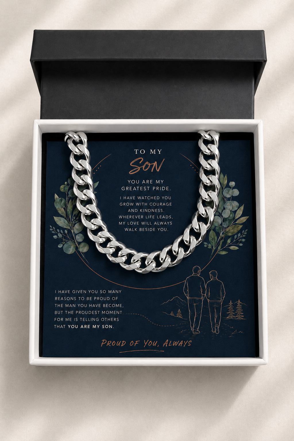 A silver chain necklace presented inside an open white gift box with a black lid, set against a light neutral background. 