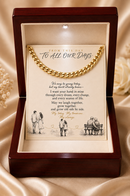 A wooden keepsake box with a dark reddish-brown finish, containing a gold chain draped over a printed sentimental letter on cream paper, set against a beige satin fabric background.
