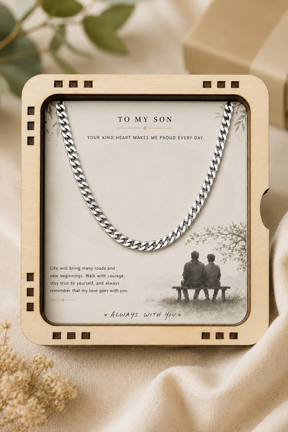 A silver curb-link chain necklace displayed inside a square beige wooden gift box with a sentimental message for a son, set against a soft beige fabric background.